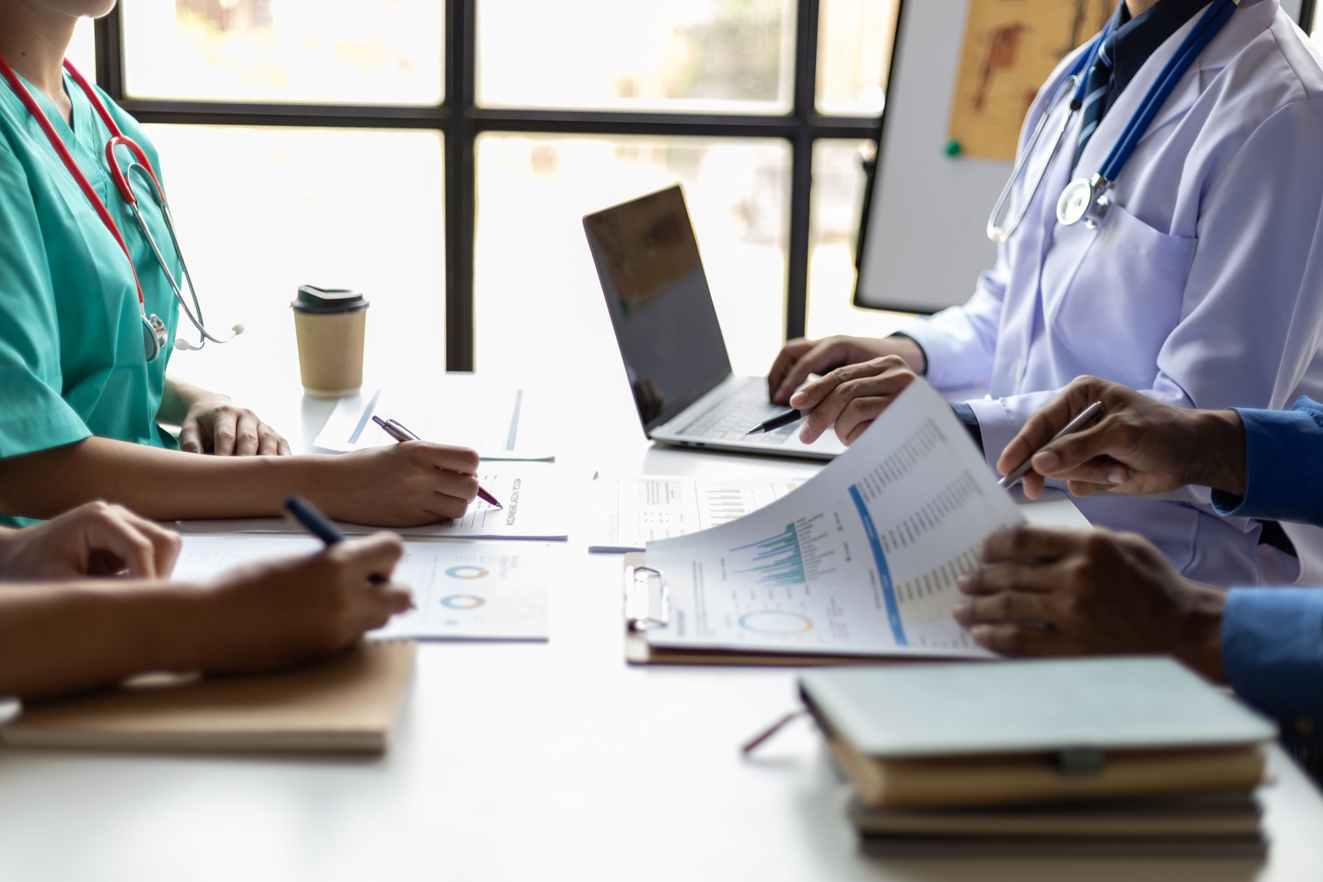 Team, medical analysts and doctors consulting with paperwork of graphs, data and charts in hospital conference room. Healthcare staff discussing statistics, results of research and innovation.